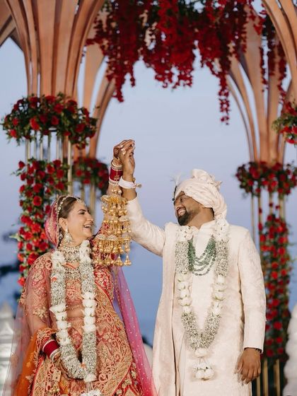 A joyous moment from the wedding ceremony, capturing the bride's traditional kaleere against the backdrop of the magnificent red floral mandap.
