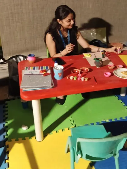 An instructor guiding children at an art and craft station during a birthday party. The setup includes kid-friendly tables, chairs, and colorful floor mats.