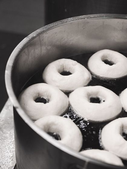 Bagels being boiled before baking, a crucial step for achieving their signature chewy texture and shiny crust.