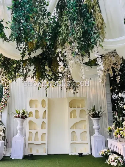 A decor detail shot showing a lush ceiling installation of hanging greens and white wisteria over a beautifully styled console table.