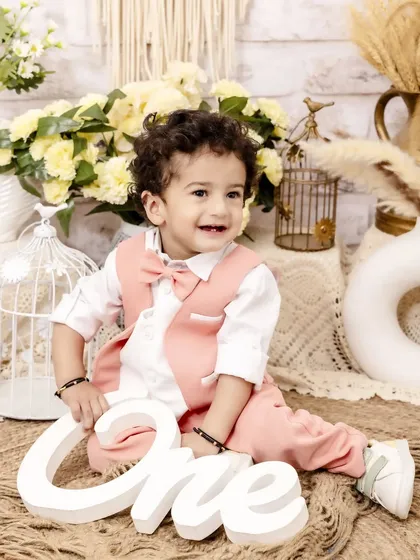Dressed in a charming pink vest and bowtie, this little boy celebrates turning one. His joyful smile is the centerpiece of this bright and happy milestone portrait.