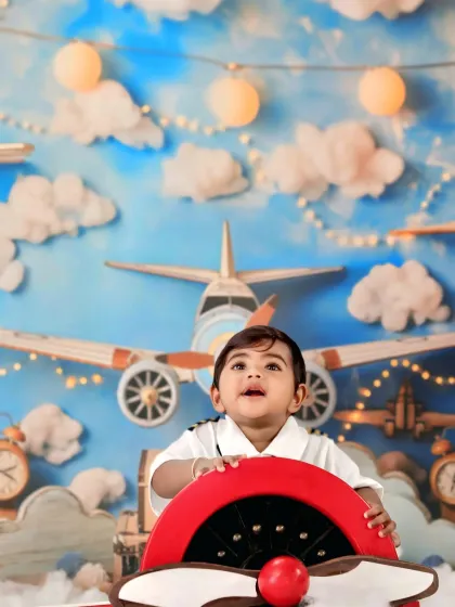 Looking up with a happy expression, this little pilot is ready for adventure at the helm of a red propeller plane.