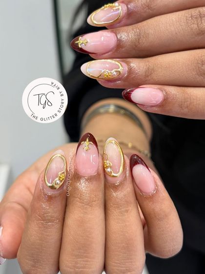 An ornate French manicure with deep maroon tips and intricate 3D gold accents. This set combines classic style with luxurious, jewelry-like details.