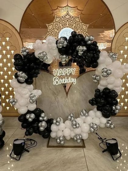 A grand and symmetrical black and white balloon decoration in a banquet hall. The central heart-shaped arch is flanked by matching balloon pillars, creating a dramatic photo backdrop.