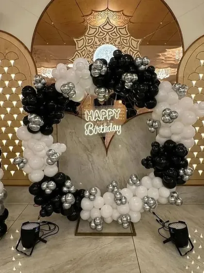 This high-contrast black and white balloon arrangement on a circular frame creates a dramatic and elegant photo backdrop. The setup includes a neon sign and can be installed in banquet halls or large living rooms for your anniversary event.