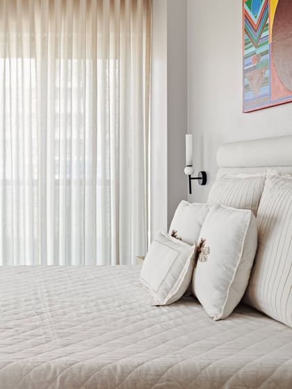 A detail of the bedding and art in the Maximum City Duplex. The clean, white linens and simple wall sconce are punctuated by a colorful piece of abstract art, reflecting the client's personal taste.