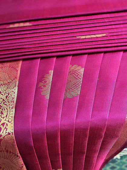 A close-up of the pleats on a magenta bridal silk saree for a client named Pooja. The precision ensures the motifs on the saree are displayed beautifully.