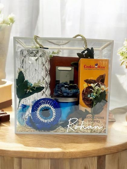 This elegant gift for a brother is presented in a clear acrylic bag, showcasing a crystal-cut lamp, a personalized frame, and other curated items in a cool blue theme.