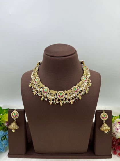 A classic antique gold necklace with circular motifs and multi-colored stones. The set includes matching jhumki earrings, making it a perfect piece for traditional wear.
