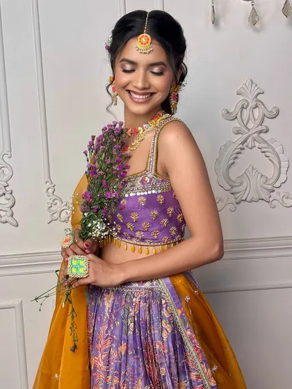 Holding flowers, this bride embodies the joyful spirit of her Mehendi. The 'Khushnuma' makeup with its pop of color and radiant finish perfectly matches the festive mood.