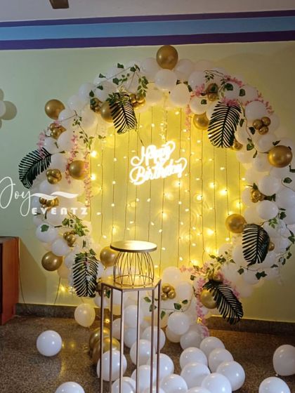 I designed this elegant balloon ring with a fairy light curtain backdrop. The arch of white and gold balloons is accented with artificial tropical leaves, creating a soft and magical look for a home party.