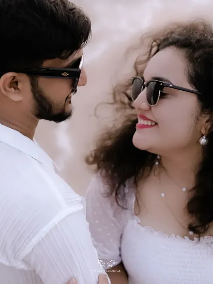 A close-up of the couple smiling at each other, their sunglasses adding a cool, stylish vibe to their beach shoot.