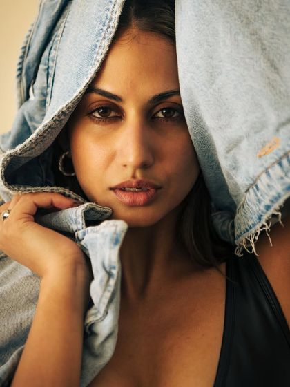 A cool and casual portrait with a denim jacket used as a prop. The way the jacket frames the face adds a layer of mystery and attitude. The lighting is natural and soft, keeping the focus on the model's direct gaze.