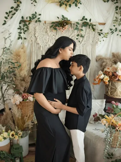 A mother's gentle kiss for her son. This touching moment is captured in our boho studio, with the contrast of the black dress against the neutral decor creating a striking and emotional image.