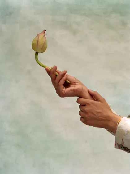 A detailed shot focusing on hands and a lotus bud. This image is part of a larger conceptual story, using simple, symbolic gestures to add a layer of artistic meaning to the fashion narrative.