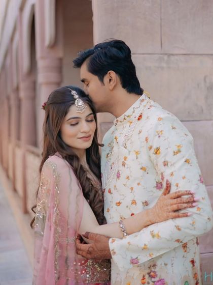 A sweet and gentle moment from a Mehendi ceremony, with the groom kissing the bride's forehead as they embrace.