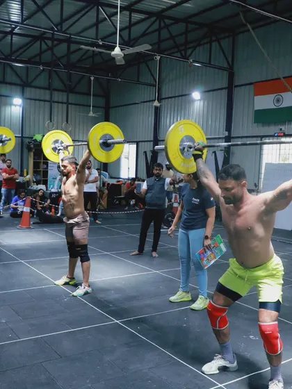 A heat of athletes performing synchronized lifts. The visual of multiple barbells going up at once is a powerful display of collective strength.