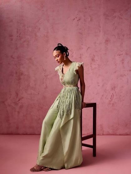 A model in a pastel green draped jumpsuit with fringe detailing on the waist, a unique and stylish choice for any event.