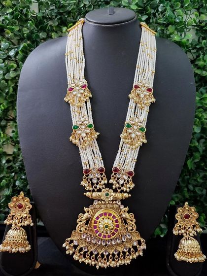 This rental set features a long, multi-strand pearl necklace with kundan motifs and a large central pendant, paired with matching jhumkas for a traditional look.