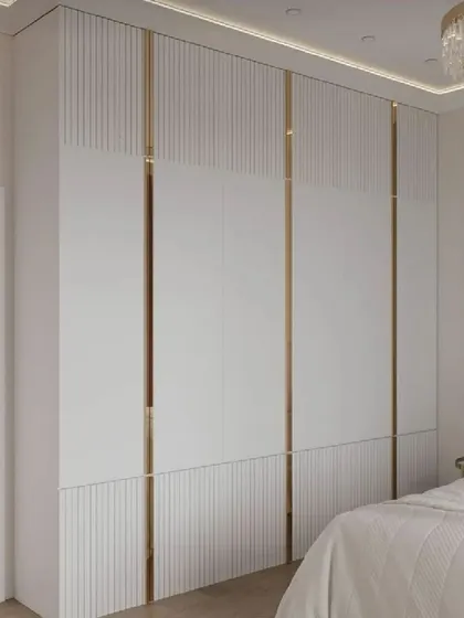 A bedroom setting featuring a white wardrobe with vertical fluting and elegant gold-toned metal inlays for a truly luxurious feel.