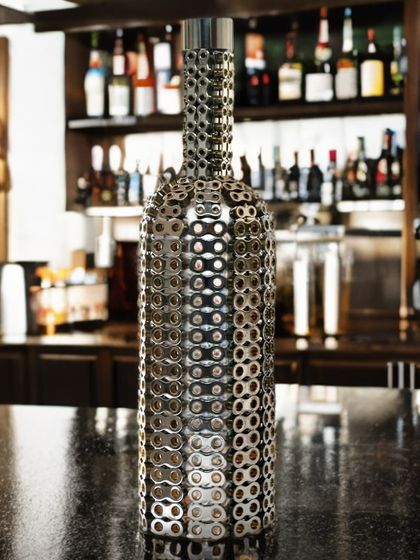 This bottle sculpture is made from hundreds of stainless steel and brass chain pieces, each stamped in a die and meticulously assembled.