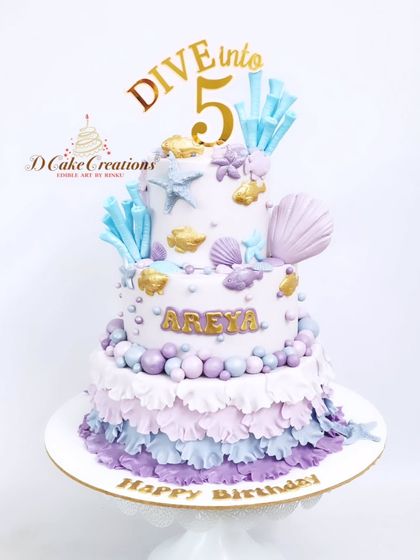 "Dive into 5" with this beautiful two-tier underwater-themed cake for Areya. The design features pastel ruffles, edible sea shells, and crystal-like sugar shards.
