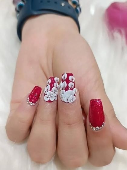 A close-up of the detailed 3D floral work on sparkling red nails, showing how each petal is carefully sculpted.