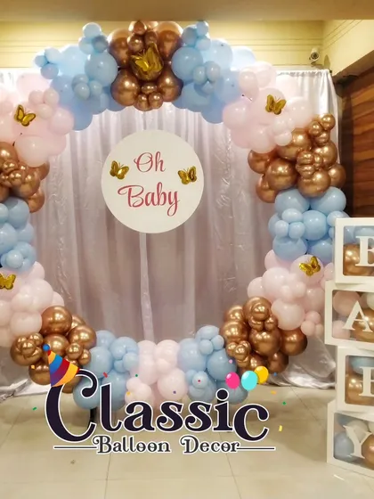A circular 'Oh Baby' photo booth made of pink, blue, and rose gold balloons. This popular design includes butterfly accents and 'BABY' blocks.