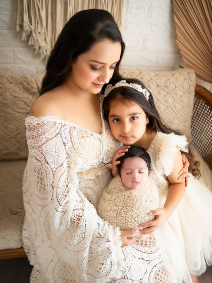 A mother's gentle embrace, holding her newborn and her older daughter close.