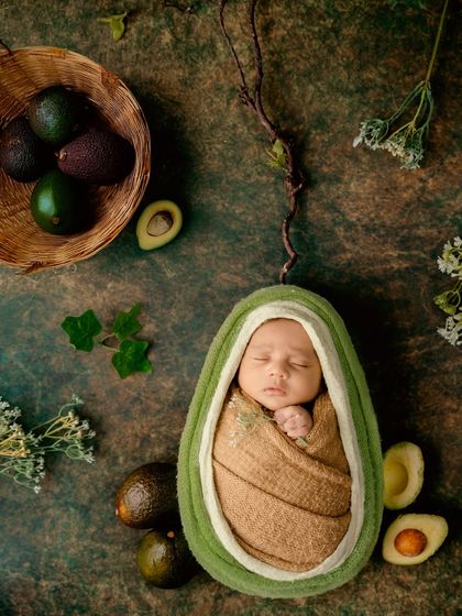 Our little "avo-cuddle." This fun and creative shot shows a newborn snugly wrapped inside a custom-made avocado prop, showcasing a playful and unique theme.