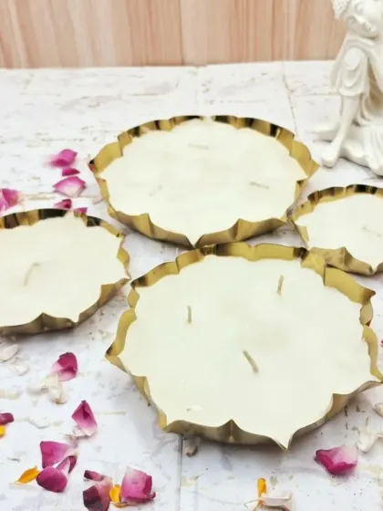 A set of four lotus-shaped brass urli candles in varying sizes, filled with plain white soy wax.