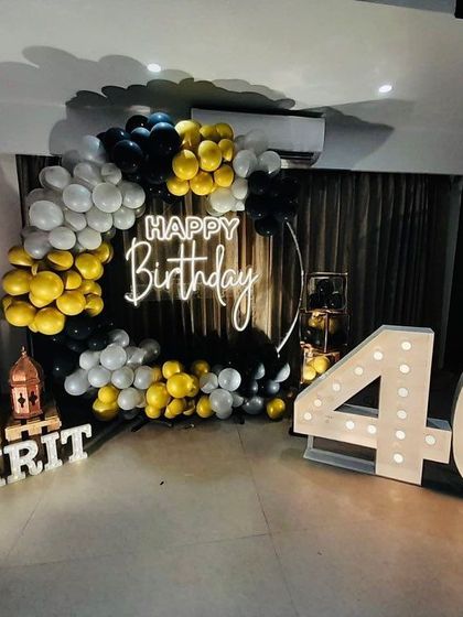 A stylish 40th birthday party with a black, gold, and white balloon ring, a neon sign, and large marquee numbers.