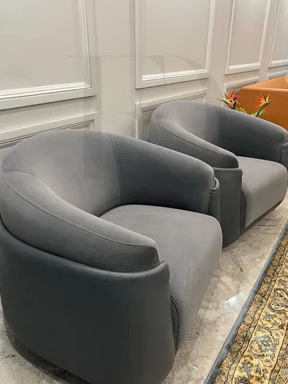 A pair of modern, curved armchairs in a two-tone grey upholstery. The design offers a comfortable, enveloping feel, perfect for creating an intimate conversation nook.