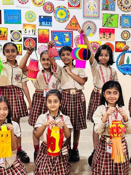 A group of girls proudly holds up their handmade lanterns against a backdrop of vibrant student artwork. Our art and craft sessions for Diwali are a highlight of the festive season.
