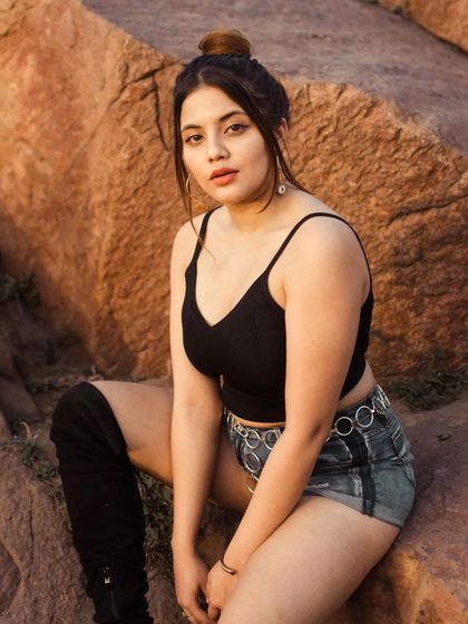 A golden hour portrait taken in a rugged, hilly area. The warm light and natural setting complement the casual styling, resulting in an authentic and relaxed outdoor photograph.