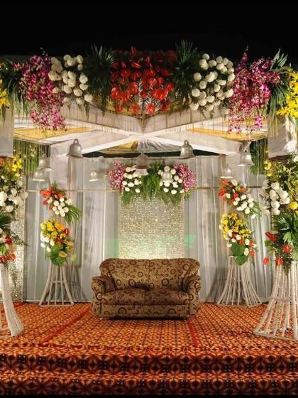 A classic wedding reception stage design. We use a combination of colorful floral arrangements on pedestals and a beautifully draped backdrop to create a timeless and elegant setting.