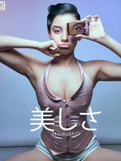 An artistic portrait with Japanese text overlay, 'utsukushii' (beauty), for a conceptual magazine feature. The image plays with the idea of self-perception using a digicam as a prop.