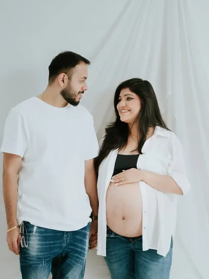 A simple and classic indoor maternity portrait. The couple's casual attire and the clean white background create a timeless look that focuses on their connection.