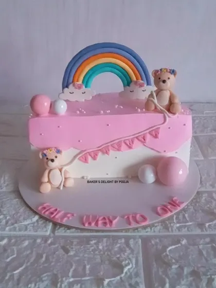 A pink and white half-birthday cake with two adorable teddy bears and a rainbow. This design is perfect for celebrating a little one being "halfway to one."