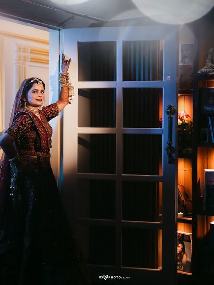 A stylish bridal portrait using dramatic lighting. The bride stands in a doorway, illuminated by a cool blue light from one side and warm light from the other, creating a high-fashion, cinematic look.