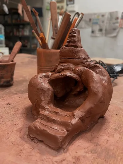 The small, hand-built temple taking shape on the worktable. You can see the texture of the coils and the marks of the tools, a testament to the hands-on process of its creation.