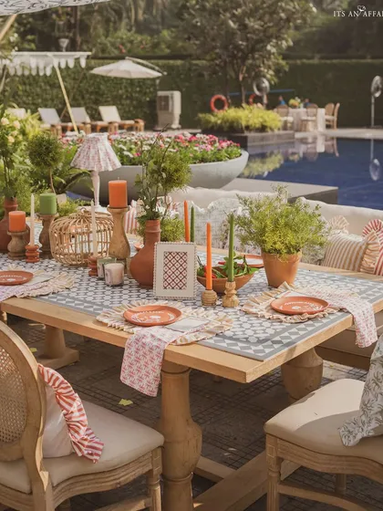 A poolside dining table, beautifully set with terracotta plates, green candles, and potted herbs.