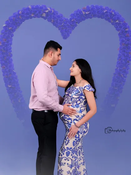 A beautiful studio portrait of a couple, with the mother-to-be in a blue and white sequined gown, framed by a heart-shaped floral graphic.