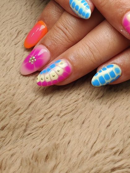 A detailed shot focusing on the textured nail art, where a base of pink and blue is overlaid with a dotted pattern and lined with delicate gold studs.