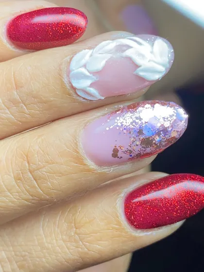 A close-up of a festive design with sparkling red nails and 3D white leaf accents.