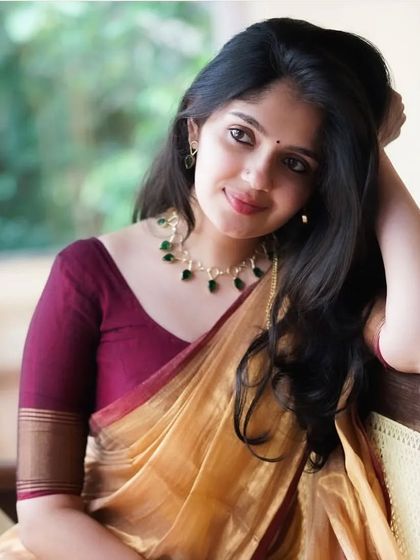 The golden tissue cotton saree is a timeless classic. Paired here with a maroon blouse and emerald necklace, it creates a look of pure elegance.