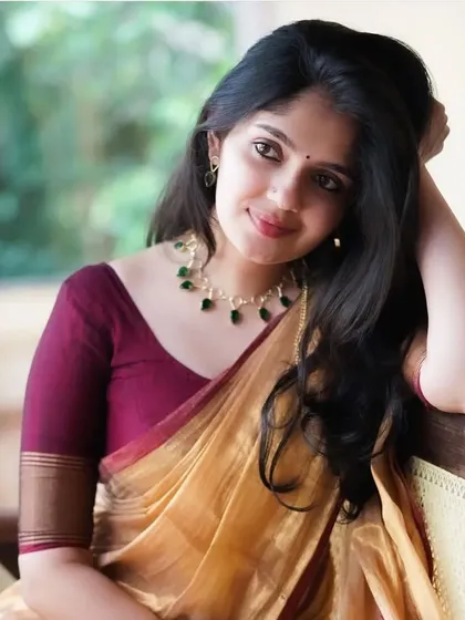 The golden tissue cotton saree is a timeless classic. Paired here with a maroon blouse and emerald necklace, it creates a look of pure elegance.