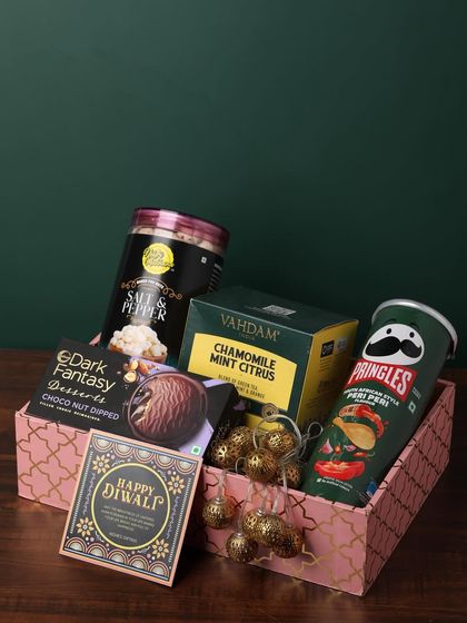 This pink-themed box is filled with a variety of gourmet snacks. It includes Pringles, Vahdam tea, dark fantasy desserts, and salt & pepper popcorn, perfect for a foodie.