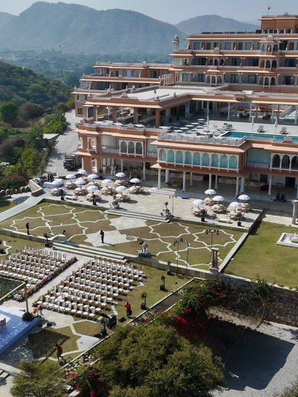 A drone shot providing a sense of the wedding's grand scale. The ceremony setup is perfectly situated within the sprawling lawns of the Udaipur palace venue, creating a truly spectacular destination wedding experience.