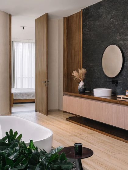 A view from the bedroom into the master bathroom, showing the open and flowing transition between the two spaces. The material palette of wood and stone continues, creating a cohesive suite.
